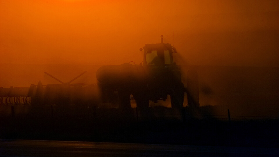 Silhouette of a farmer driving a tractor with a red sky