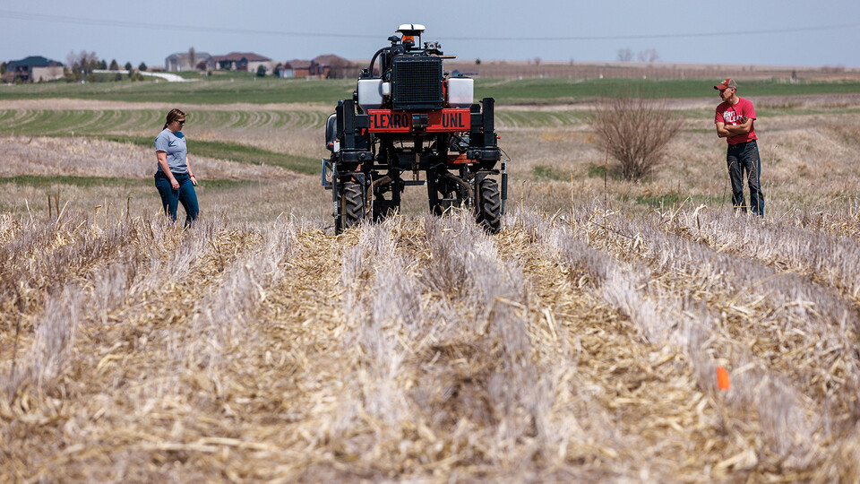 A man and a woman walk behind the Flex-Ro autonomous planting robot in a field.