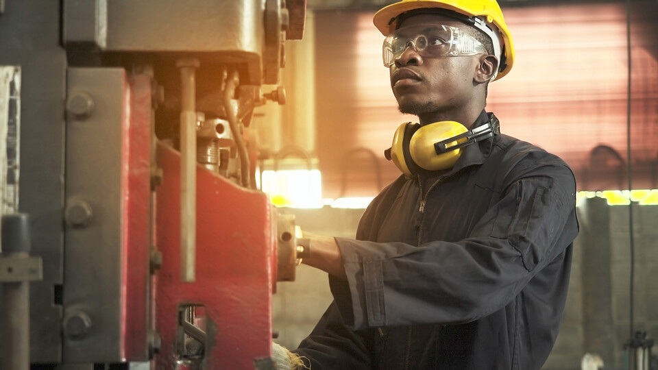 A young man wearing a hard hat and safety goggles operates a machine.