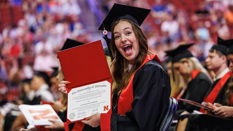 A young woman in graduation regalia excitedly displays her newly earned degree.
