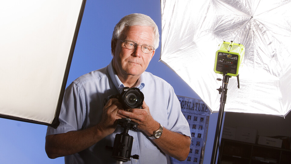 Tom J. Slocum holds a camera with lighting equipment in the background.