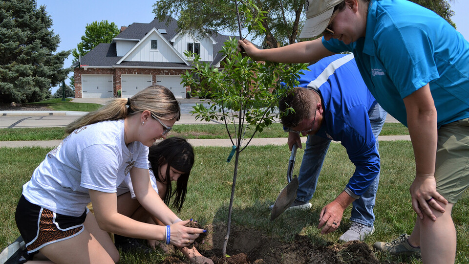 Two Wahoo Public Schools students join Josh Synder, director of learning for the school district, and Sarah Buckley, sustainable landscape coordinator for the Nebraska Statewide Arboretum, in planting trees on the grounds of Wahoo High School.