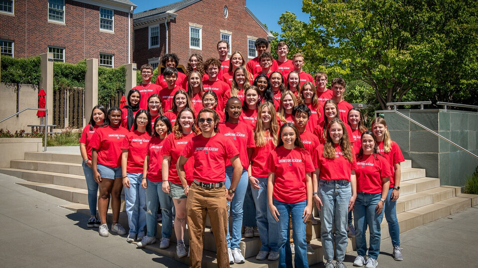 A large group of Nebraska Engineering students, wearing red T-shirts, stands outside of the Wick Alumni Center.