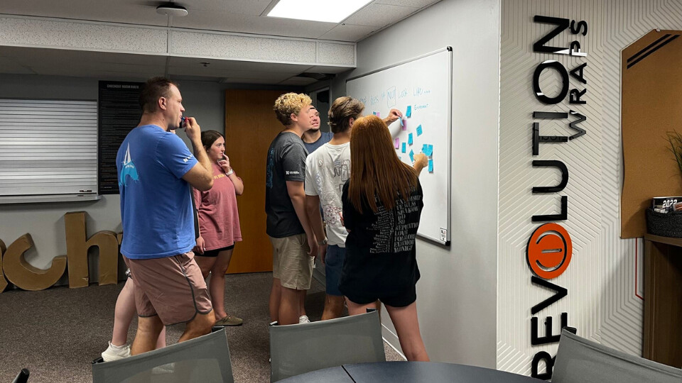 A group of students looks at sticky notes on a markerboard.
