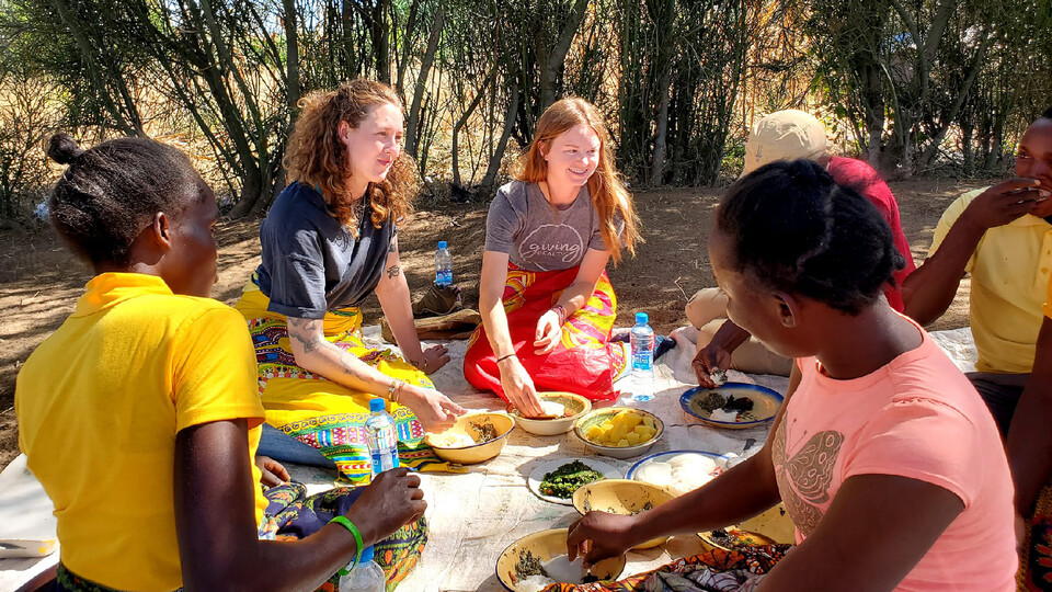 Claire Gillespie and Katie Schmitz dine with Zambians on a blanket.
