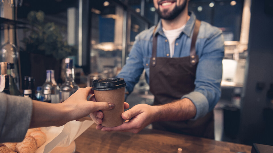 A male barista hands a woman a cup of coffee.