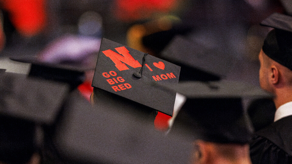A mortar board with the words "Go Big Red" and "I (Heart) Mom" is seen among Husker graduates.