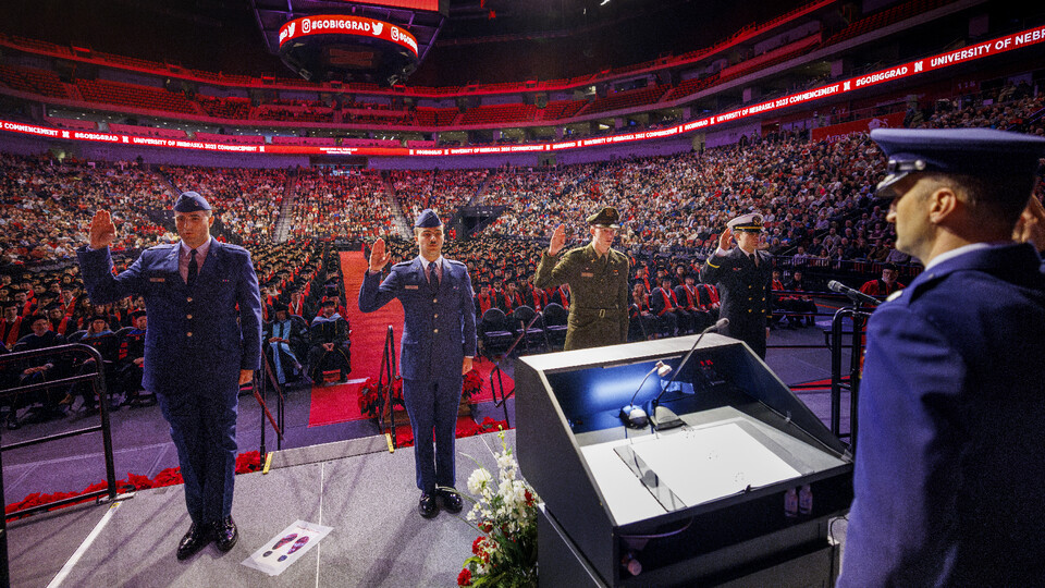 Four ROTC members recite the oath of enlistment on stage at undergraduate commencement.