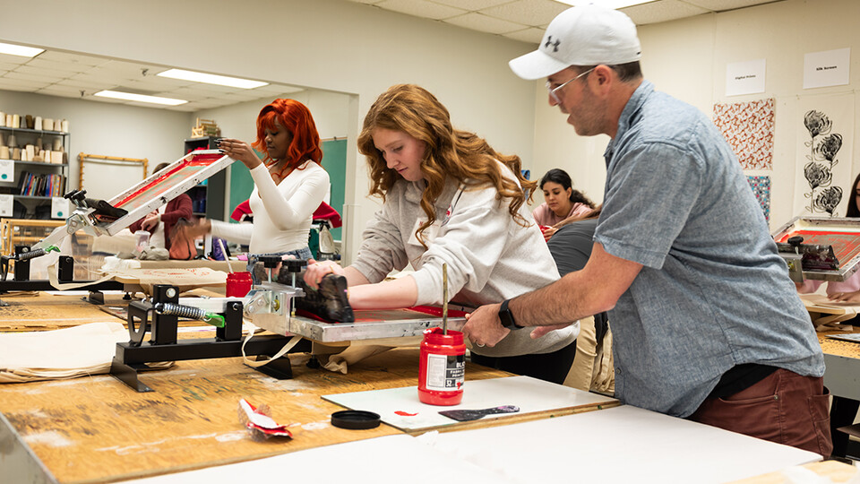 Michael Burton, assistant professor of art and design, assists a visiting high school student with a screen printing project during the TMFD Expo.