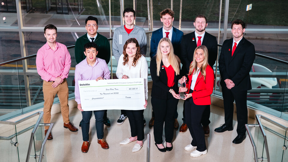 Ten students pose with a giant check and a glass trophy on a staircase.