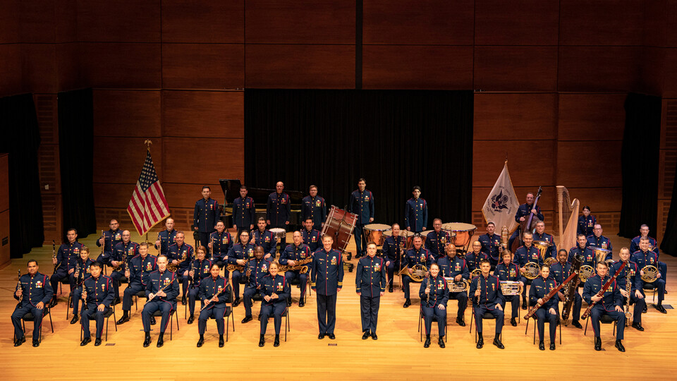 The U.S. Coast Guard Band appears on stage in uniform, with instruments.