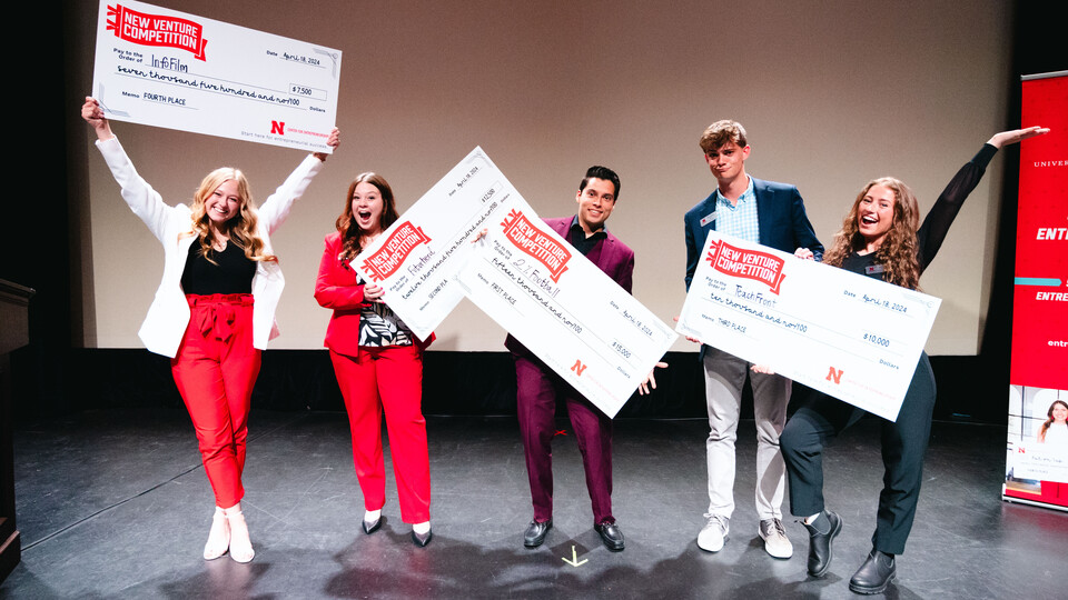 Three young women and two young men hold giant checks on a stage.