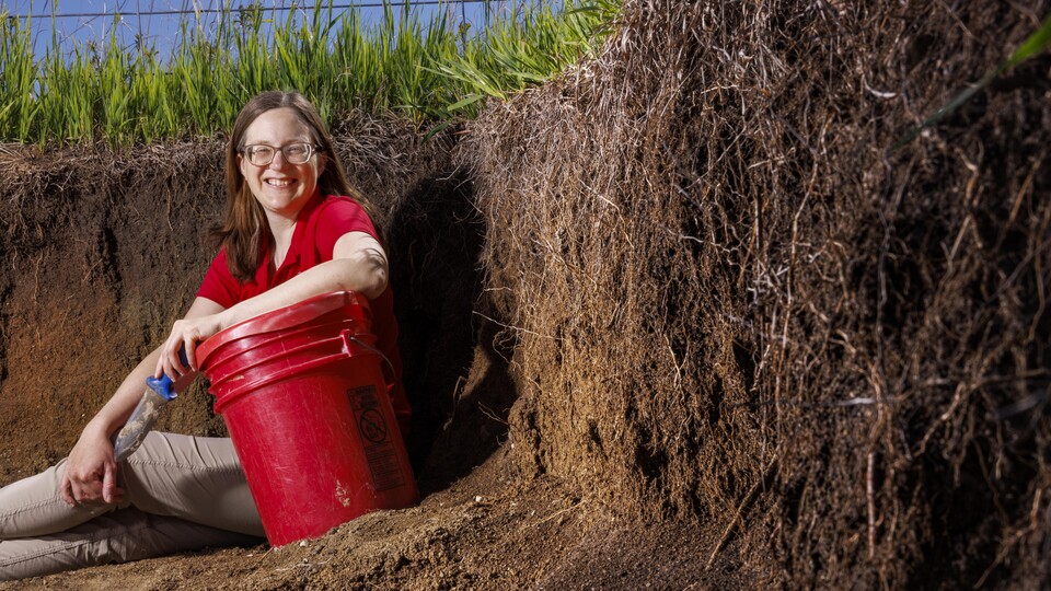 Judith Turk sits with a red bucket near exposed topsoil.