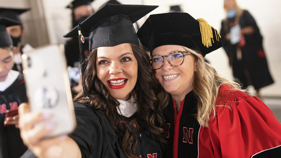 Nicole Blackstock (right) poses for a selfie with Whitney Jurgens before graduate commencement on Aug. 13, 2021. Blackstock has served for nearly 10 years in the College of Journalism and Mass Communications. Her work is conducted mostly behind scenes and keeps the college and its students maintain momentum.