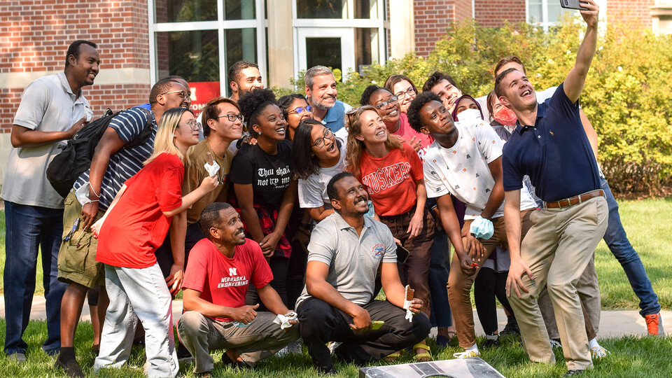 A large number of international students pose for a group selfie outdoors during an ice cream social event.