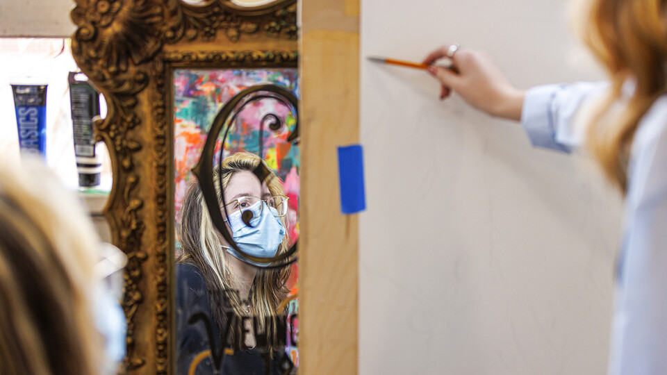 Framed by a mirror in a Richards Hall studio, Elisa Dorsey discusses a sketch by Caitlin Hoppe. The student discussion was part of an intermediate painting course led by Aaron Holz, professor of art.
