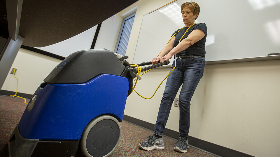 Nebraska's Tracy Oehlerking cleans the carpet below a desk in a Schorr Center meeting room on March 25. After careers in cosmetology and real estate, Oehlerking found her passion helping keep campus spaces clean for students, faculty and staff.