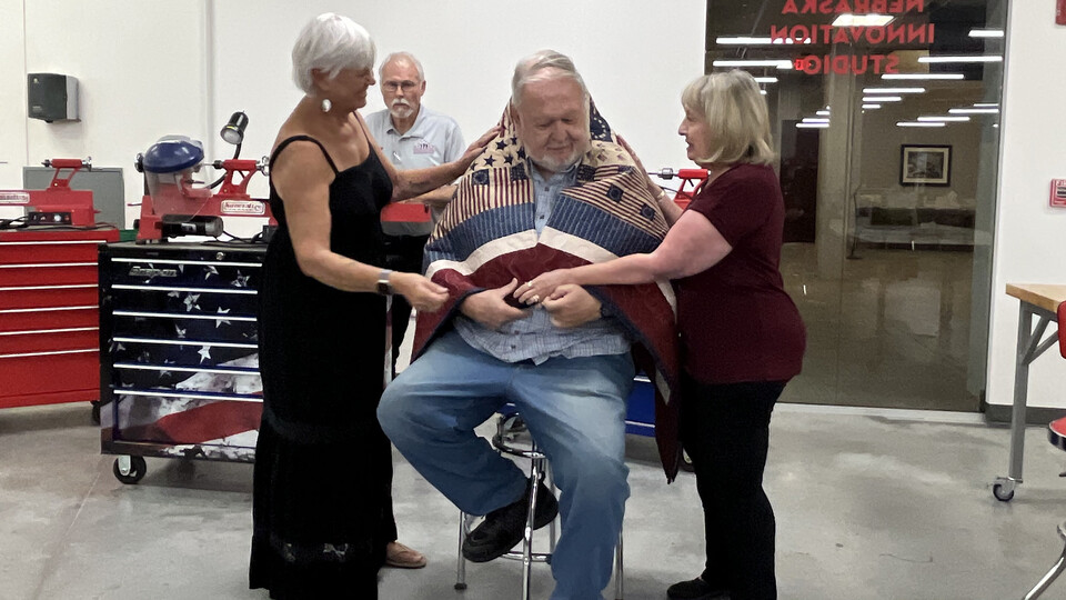 Jim Young (seated) is wrapped in his quilt from the Quilts of Valor Foundation by his sister-in-law, Pat Young, and wife, Victoria, while Doug Krapke of Fairbury looks on.