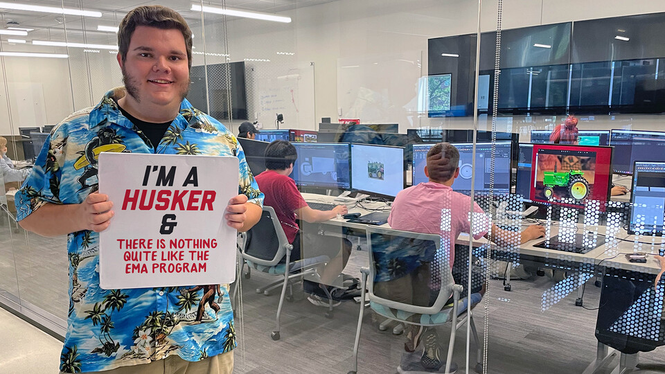 Image of Justin Watt, a first-year emerging media arts student, holding a sign that says, "I'm a Husker and there is nothing quite like the EMA program." 