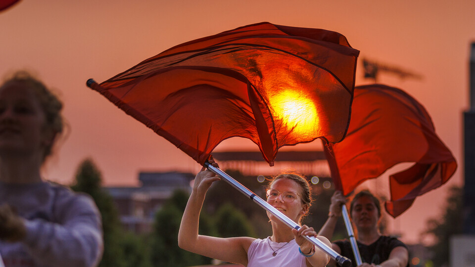 The rising sun appears to burn a hole through the flag of Cornhusker Marching Band color guard member Jaedynn Shively, a sophomore from Lincoln. 