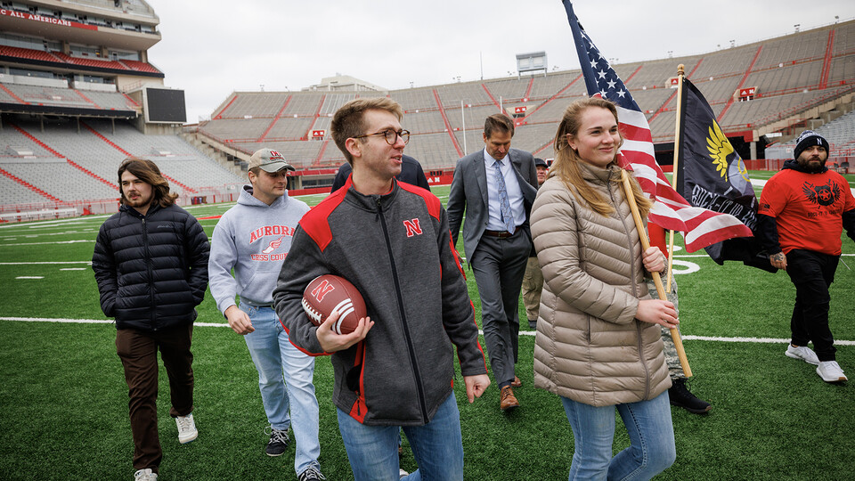 Everett Bloom (center, holding football) leads a group of student veterans, volunteers and Trev Alberts off the Memorial Stadium turf following a ceremonial beginning to the ruck march on Nov. 15. Bloom, a four-year Navy veteran, is one of the student-veteran organizers of the 2022 march.