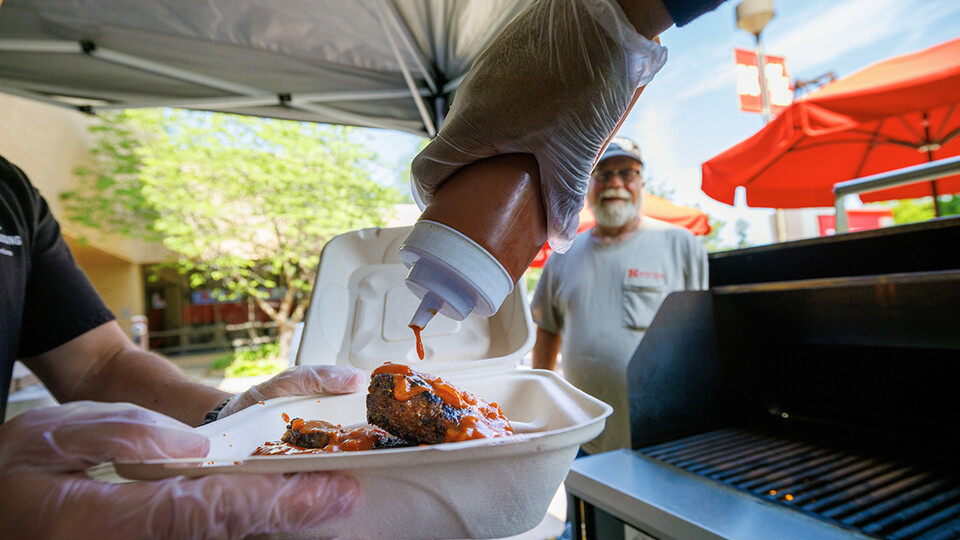 Sean Jones, a line cook with dining services, adds Oklahoma BBQ sauce to Jeff Logans order of ribs and sausages.