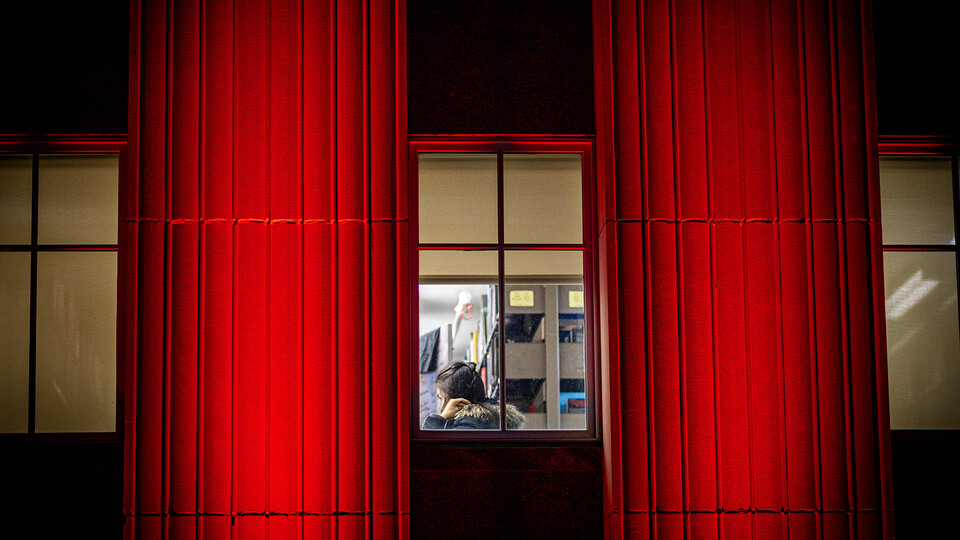 A student studies inside Love Library as red light reflects off the building's southern facade.