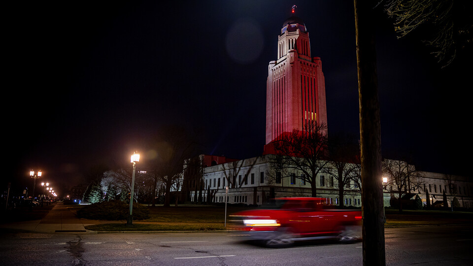 A red truck streaks down the street as the Nebraska State Capitol building glows red on Feb. 14.