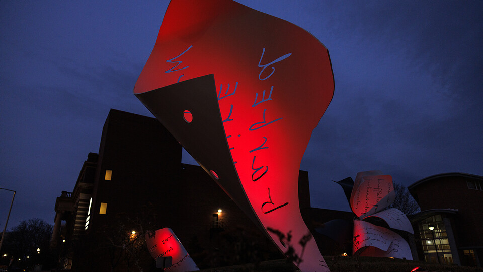 Red lights reflect off the "Torn Notebook" sculpture on UNL's City Campus.