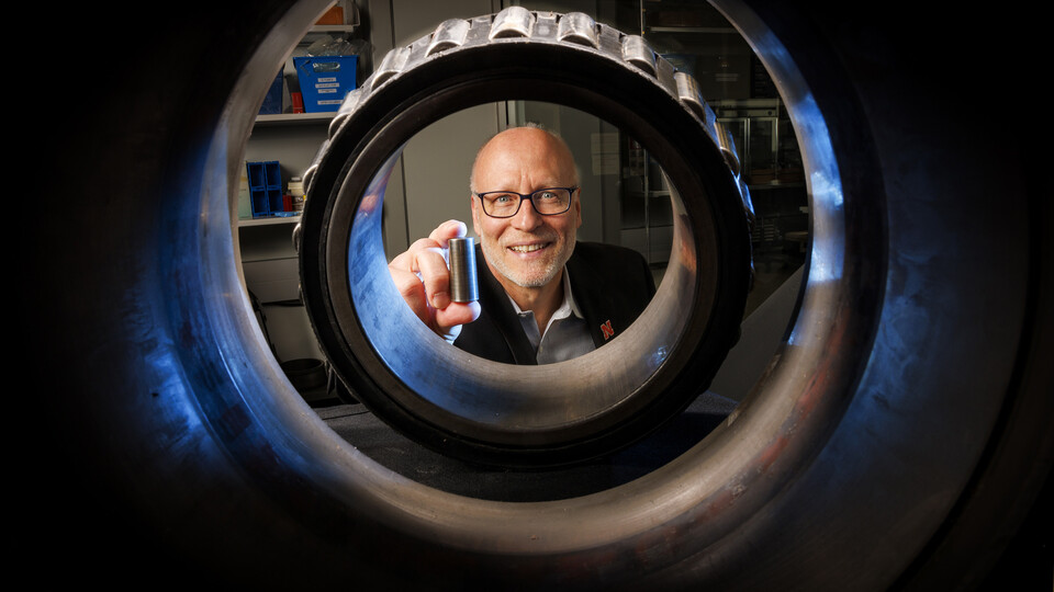 Joe Turner holds a 3D printed railcar bearing. He is photographed through an actual bearing and housing that fits on the end of each axle of a railcar axle.
