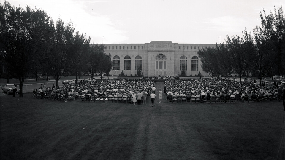 Graduates, faculty, staff, friends and family gather in what was a green space on the east side of Memorial Stadium for commencement exercises on Aug. 3, 1962. The university has hosted commencement in numerous locations, adding inside Memorial Stadium on May 8.