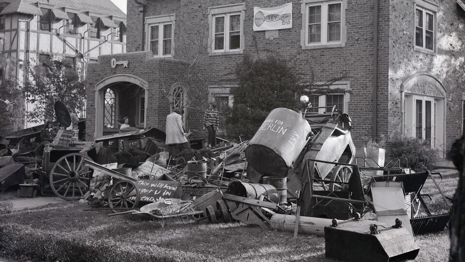 Students walk through scrap items collected outside of a Greek house during a scrap collection drive held as part of homecoming activities in 1942.
