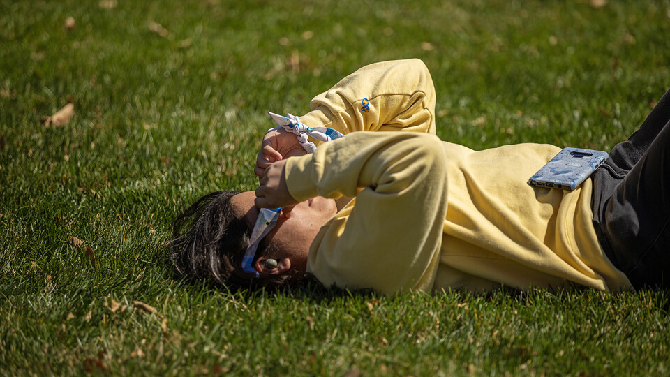A student relaxes on the East Campus Mall grass as they look skyward at the eclipse.
