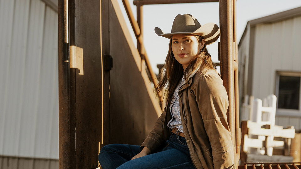 University of Nebraska–Lincoln alumna Anna Kobza sits in front of a cattle chute on her family farm.