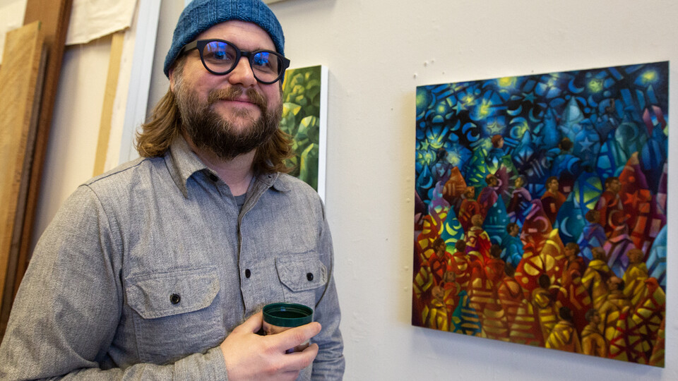 Art professor Byron Anway stands next to one of his paintings while holding a cup of coffee in his Richards Hall studio.