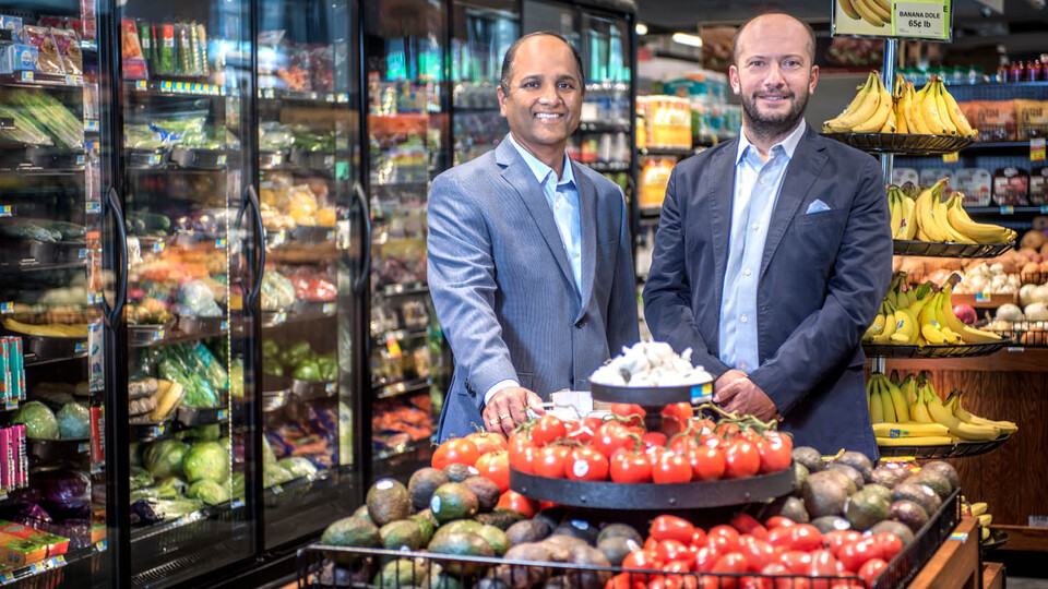 S. Sajeesh and Özgür Araz are photographed in a produce section of a grocery store.