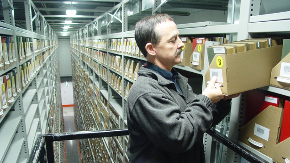 Gary Dolan looks for a book 30 feet in the air at the Library Depository Retrieval Facility on East Campus. A specialized, 8,500 pound order picker allows workers to traverse the towering aisles of books, retrieving them for patrons to review.