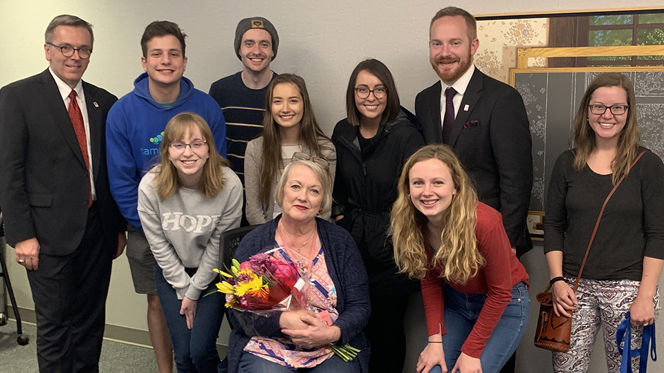 Chancellor Ronnie Green (left) and Huskers who have earned major fellowships gathered to celebrate the work of Laura Damuth (seated, with flowers) on April 18. Emily Johnson (hands on knees, at right) helped with the surprise by scheduling a meeting with Damuth.