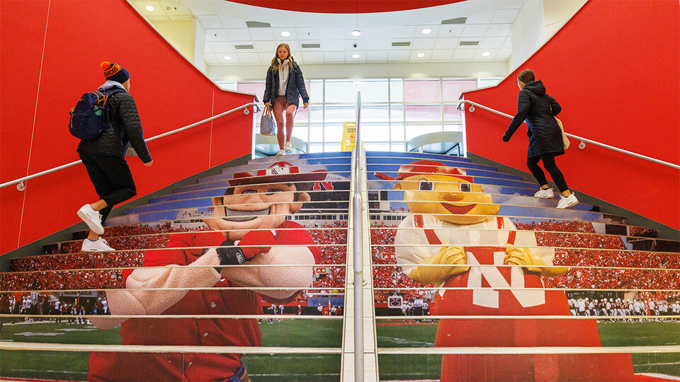 Students on staircase covered with images of Herbie Husker and Lil' Red