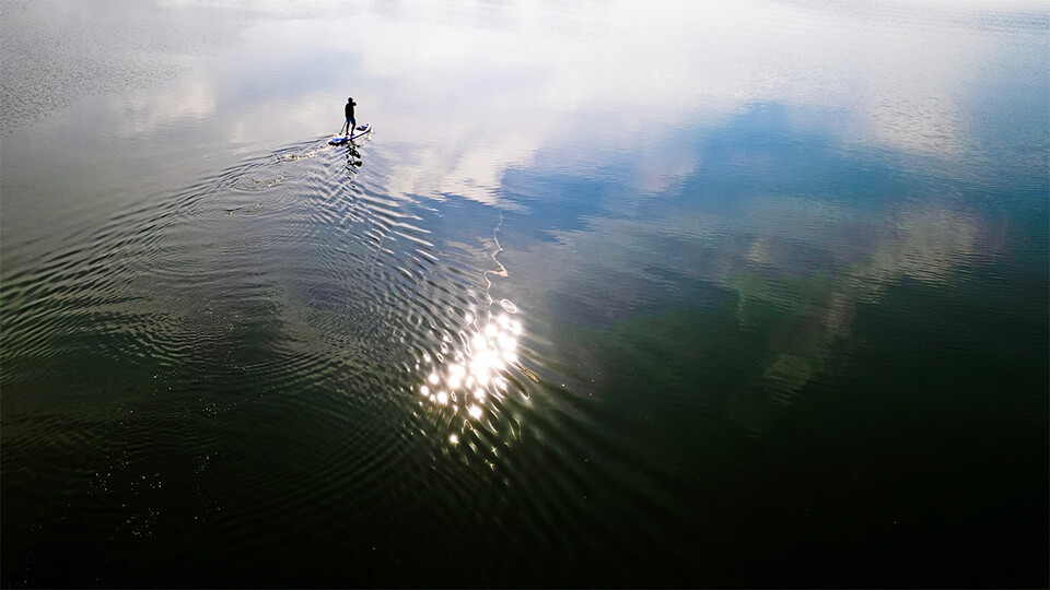 A distant shot of a silhouetted Richard Moberly paddleboarding across a lake
