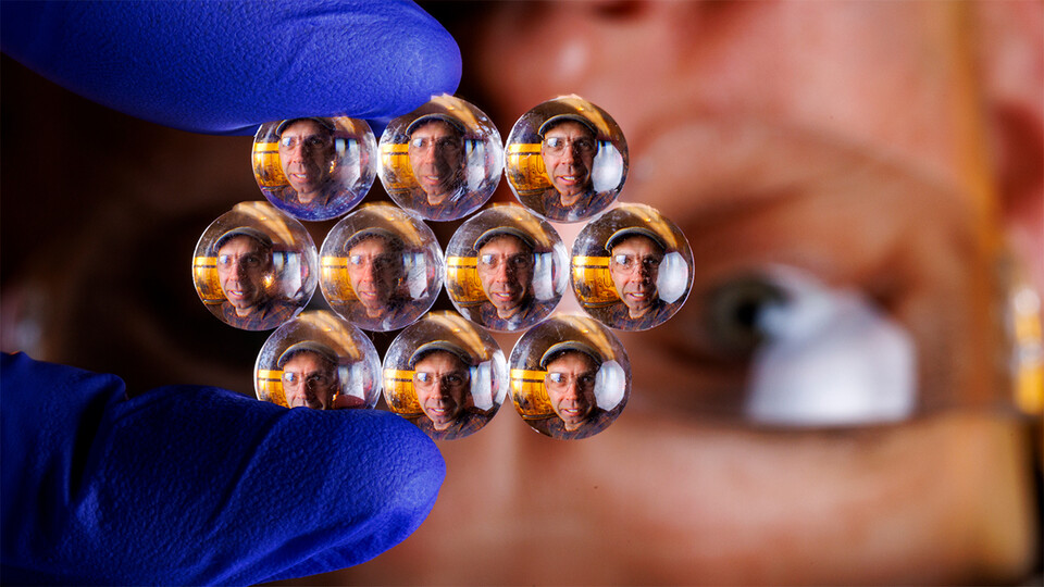 The face of Stephen Morin appears in a honeycombed array of tiny lenses that he holds between gloved fingers