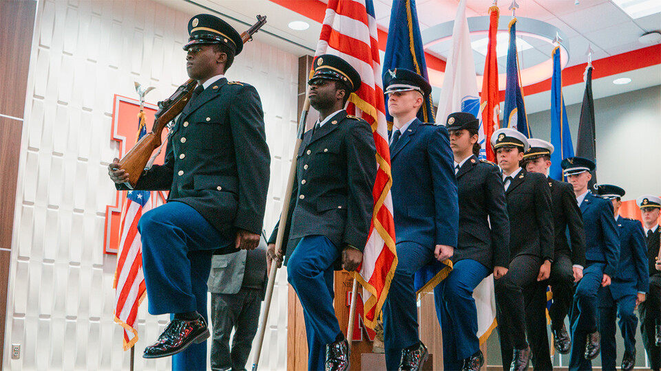 Uniformed members of the ROTC Joint Color Guard march in single file while holding flags