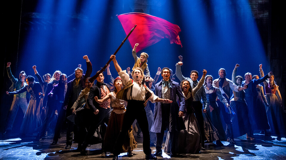 Photo of the Les Miserables cast singing and raising fists and a flag.