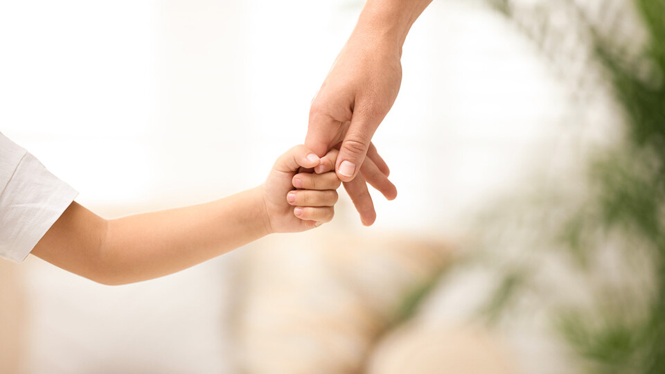 A parent holds a child's hand.