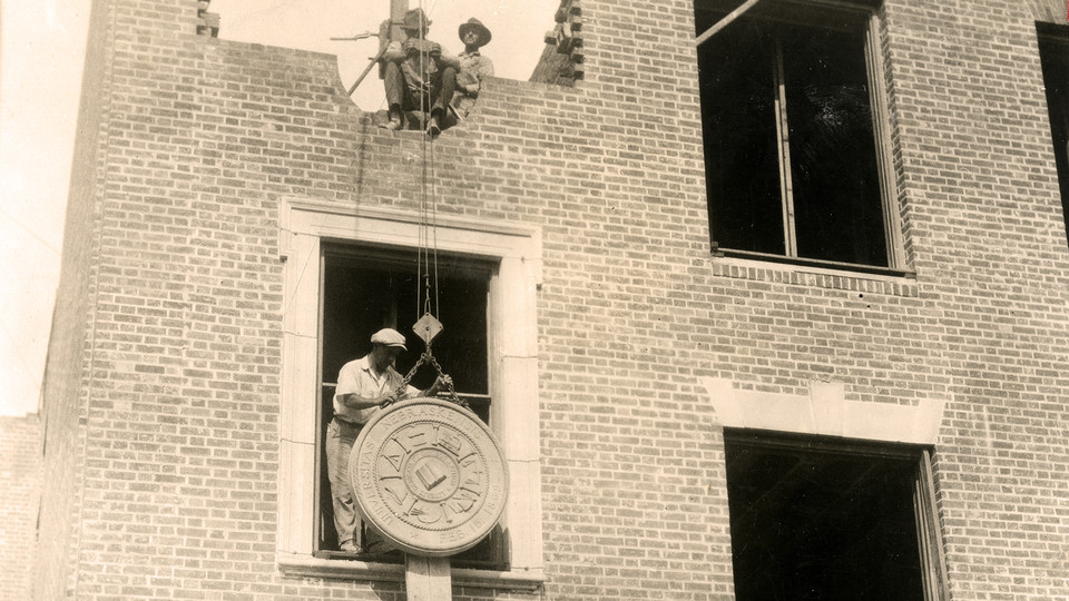 Construction workers raise a university seal into place into the east wall of Morrill Hall during construction in 1927. The building is home to the University of Nebraska State Museum.