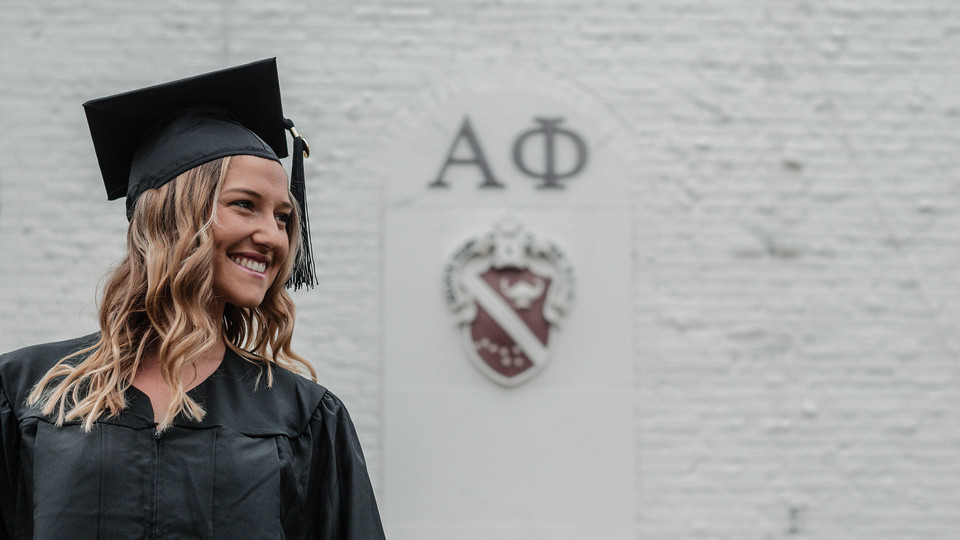 Reilly Pogue stands in her cap and gown in front of Alpha Phi.
