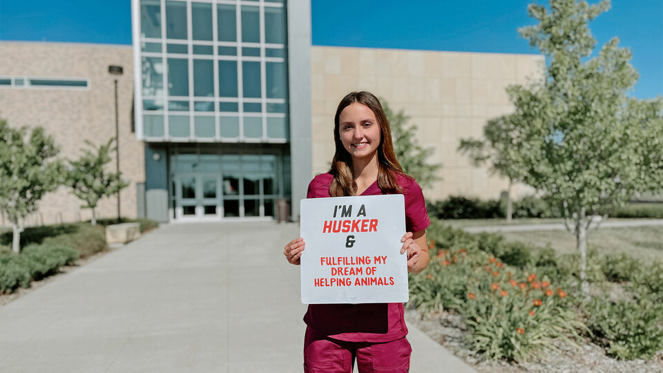 Photo of Sydney Meyer, a veterinary medicine major holding an I'm a Husker and sign on campus.