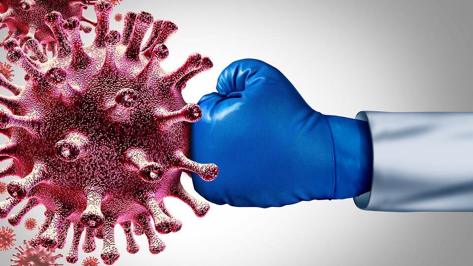 Doctor wearing a blue boxing glove punching a COVID-19 model.