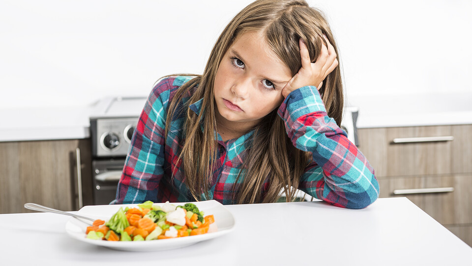 Child with head in hand looking angry about having to eat their vegetables.