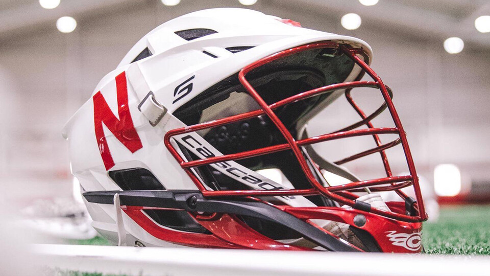 Photo of a white lacrosse helmet with a red Nebraska "N" resting on the turf of Cook Pavilion.